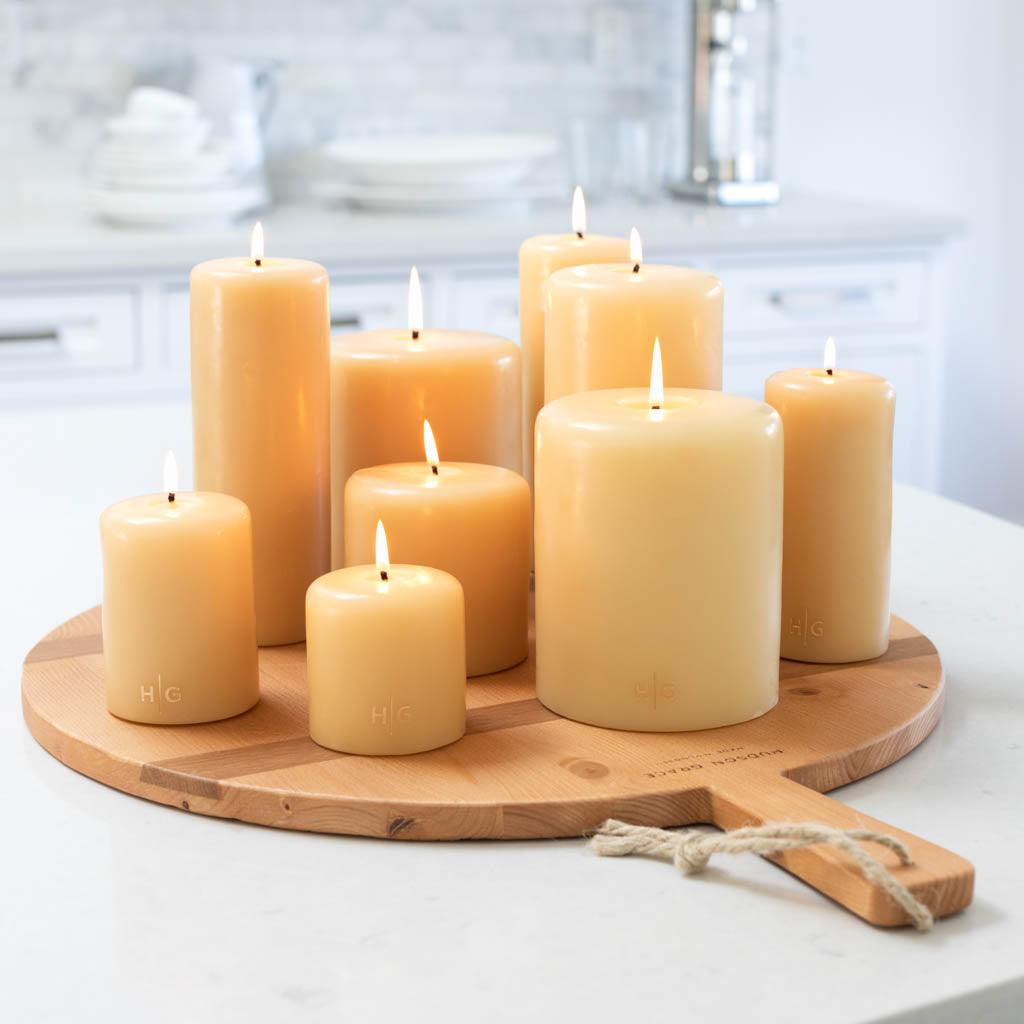 HG Amber Unscented Pillar Candles, various sizes, with gold HG logo, on a wooden serving board.