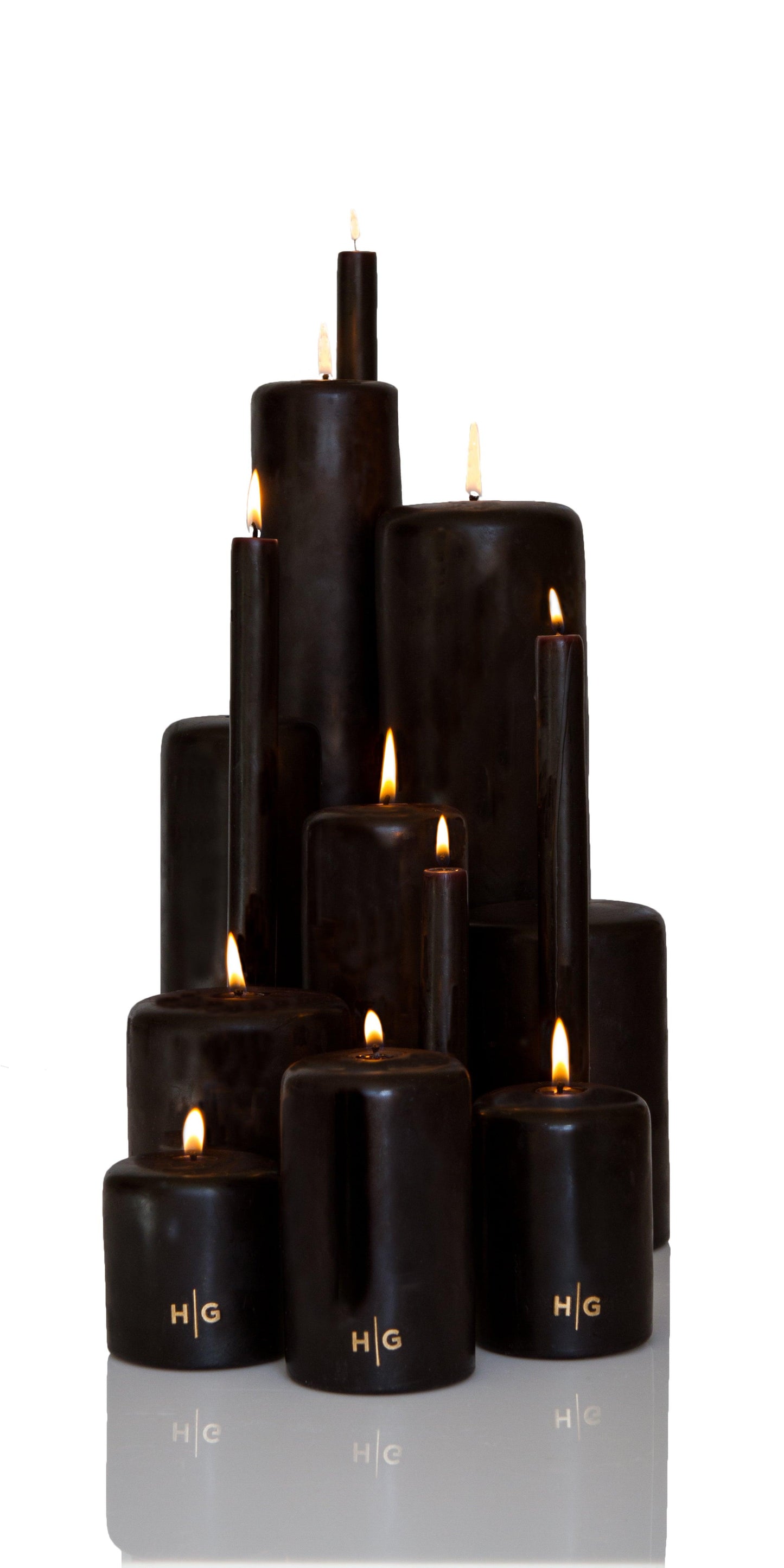HG Black Unscented Pillar Candles, various sizes, with gold HG logo and lit wicks.