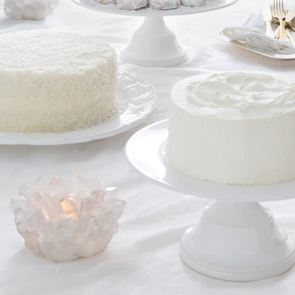 Small white ceramic pedestal cake stand with a frosted cake.