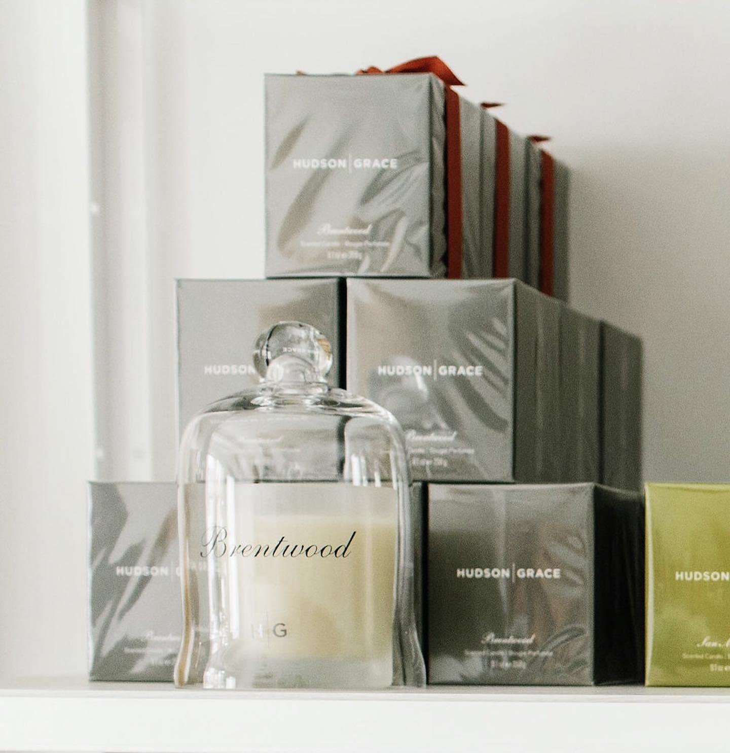 Hudson Grace Brentwood Votive Candle in clear glass cloche, surrounded by gray gift boxes with red ribbons.