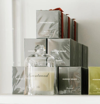 Hudson Grace Brentwood Votive Candle in clear glass cloche, surrounded by gray gift boxes with red ribbons.