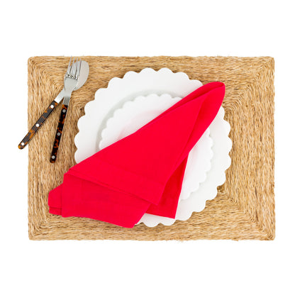Natural abaca woven rectangular placemat with white scalloped plates, red napkin, and tortoise-handle flatware.