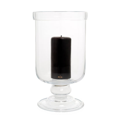 Large clear glass footed chalice hurricane candle holder with a black pillar candle inside.