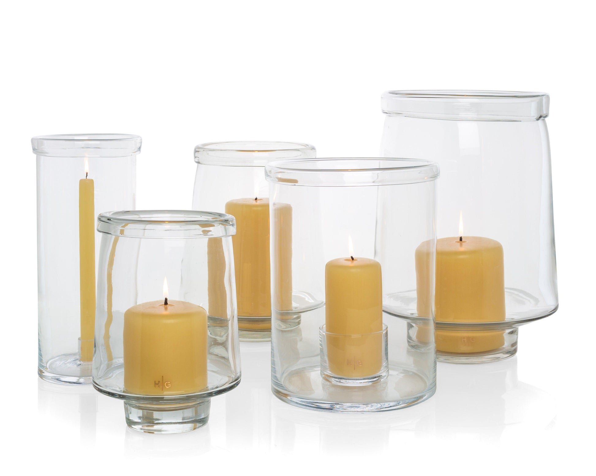 Clear glass Antwerp hurricane candle holders in three sizes, some with lit yellow pillar candles.