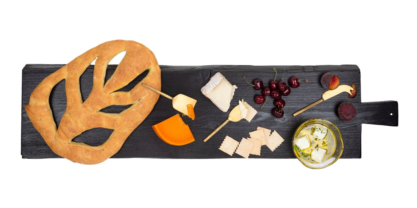Large black wood brasserie serving plank with bread, cheeses, cherries, and fruit.