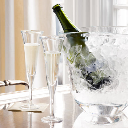 Two clear, scissor-cut glass champagne flutes with bubbly, next to a bottle in an ice bucket.