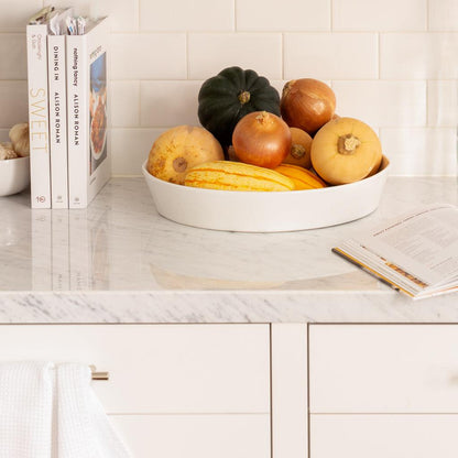 White ceramic Luce serving dish filled with colorful gourds and onions on a marble counter.