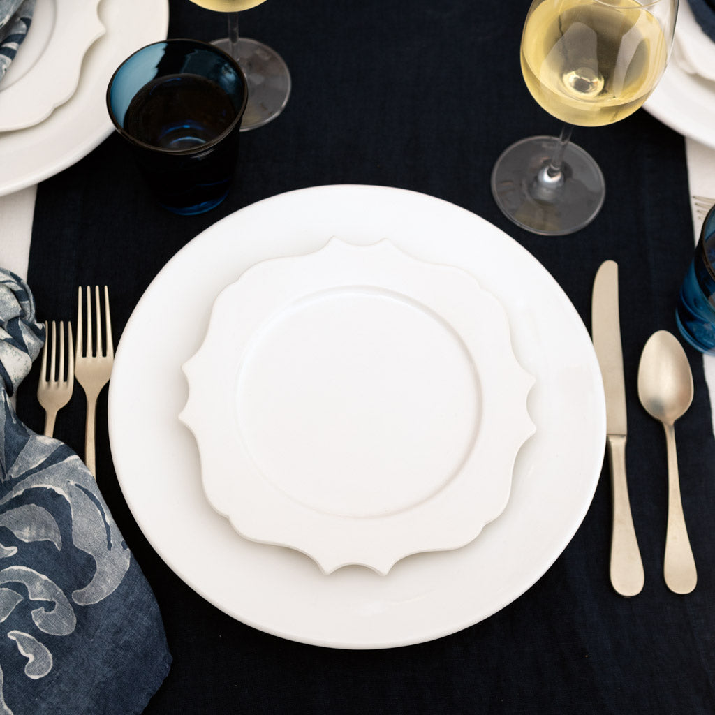 White ceramic Lungarno salad/dessert plate with sculptural edge on a dark blue table setting.
