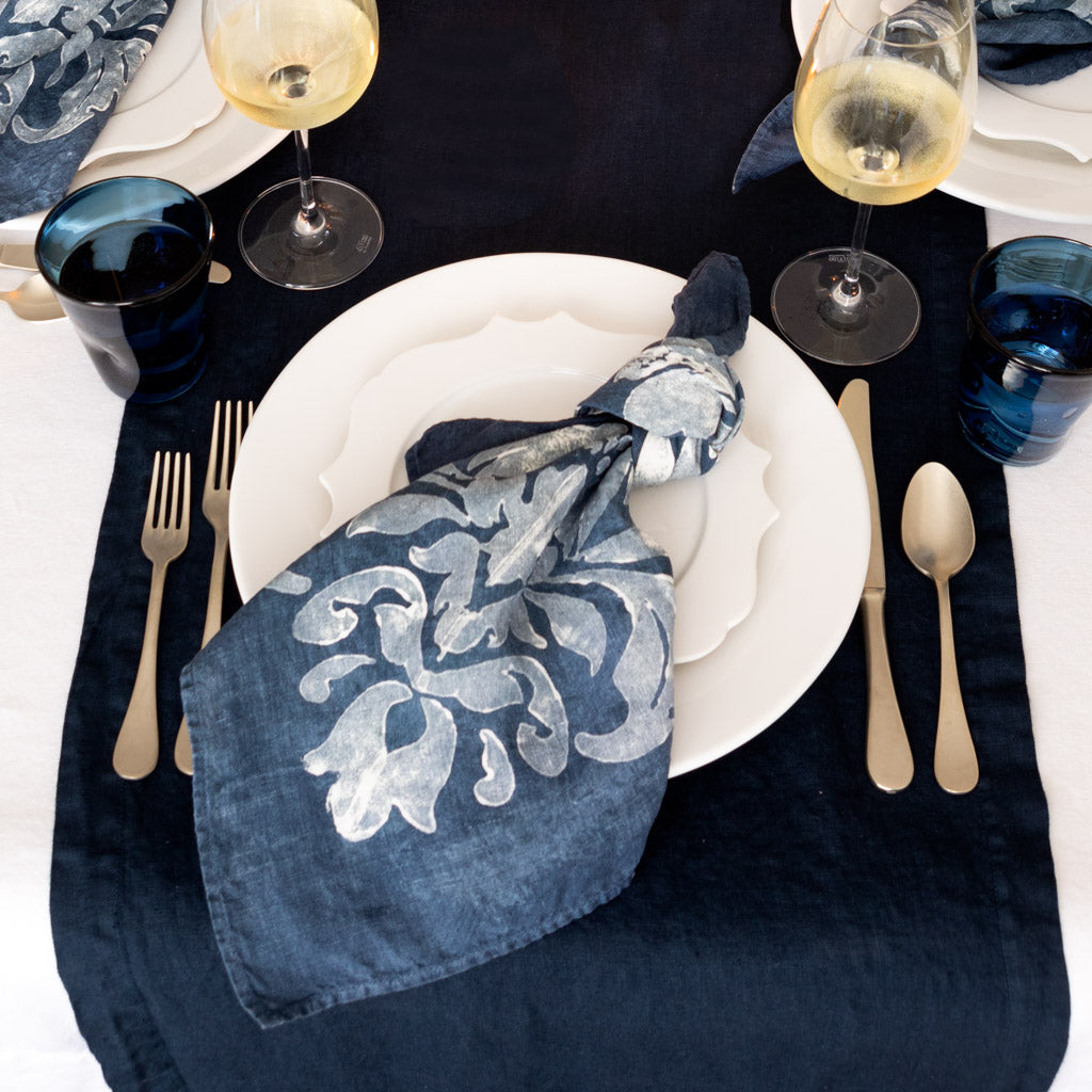 White Lungarno ceramic salad/dessert plate with sculptural rim, set on a dark blue runner with a patterned napkin.