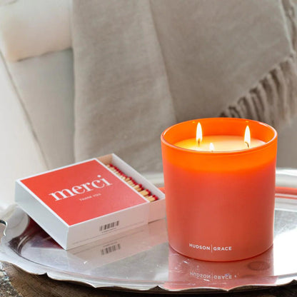 Hudson Grace "Merci" boxed matches and a lit orange candle on a silver tray.
