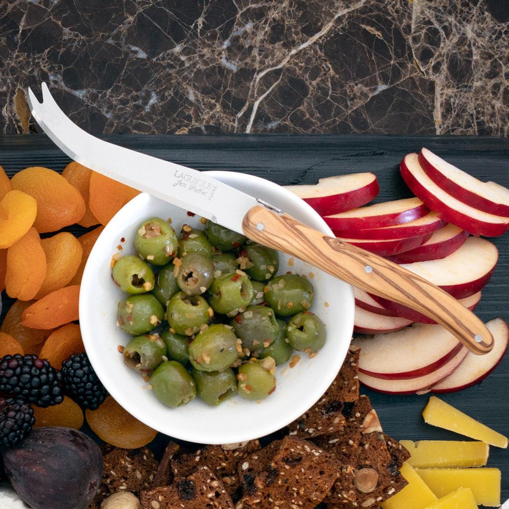 White ceramic dipping bowl filled with green olives, surrounded by fruit, crackers, and cheese.