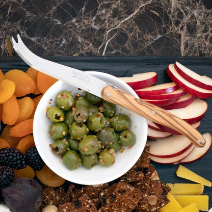 White ceramic dipping bowl filled with green olives, surrounded by fruit, crackers, and cheese.