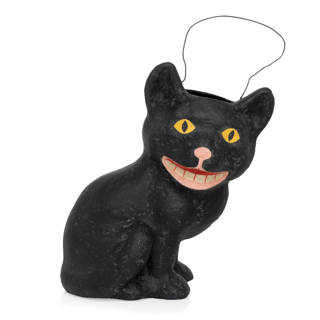Vintage-style black cat papier-mâché Halloween candy bucket with yellow eyes, a wide toothy grin, and wire handle.