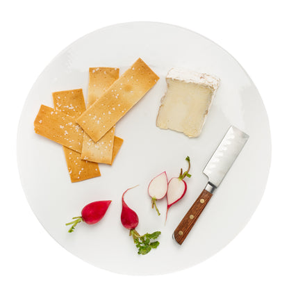 White round ceramic serving platter with crackers, cheese, radishes, and a knife.