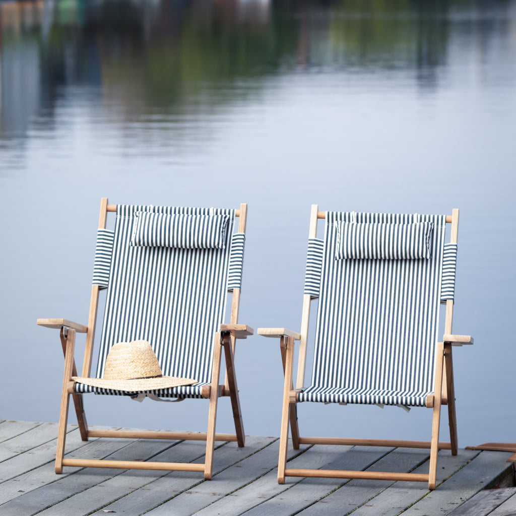 Two Navy and White Stripe Canvas Reclining Outdoor Beach Chairs with teak frames on a dock by water.