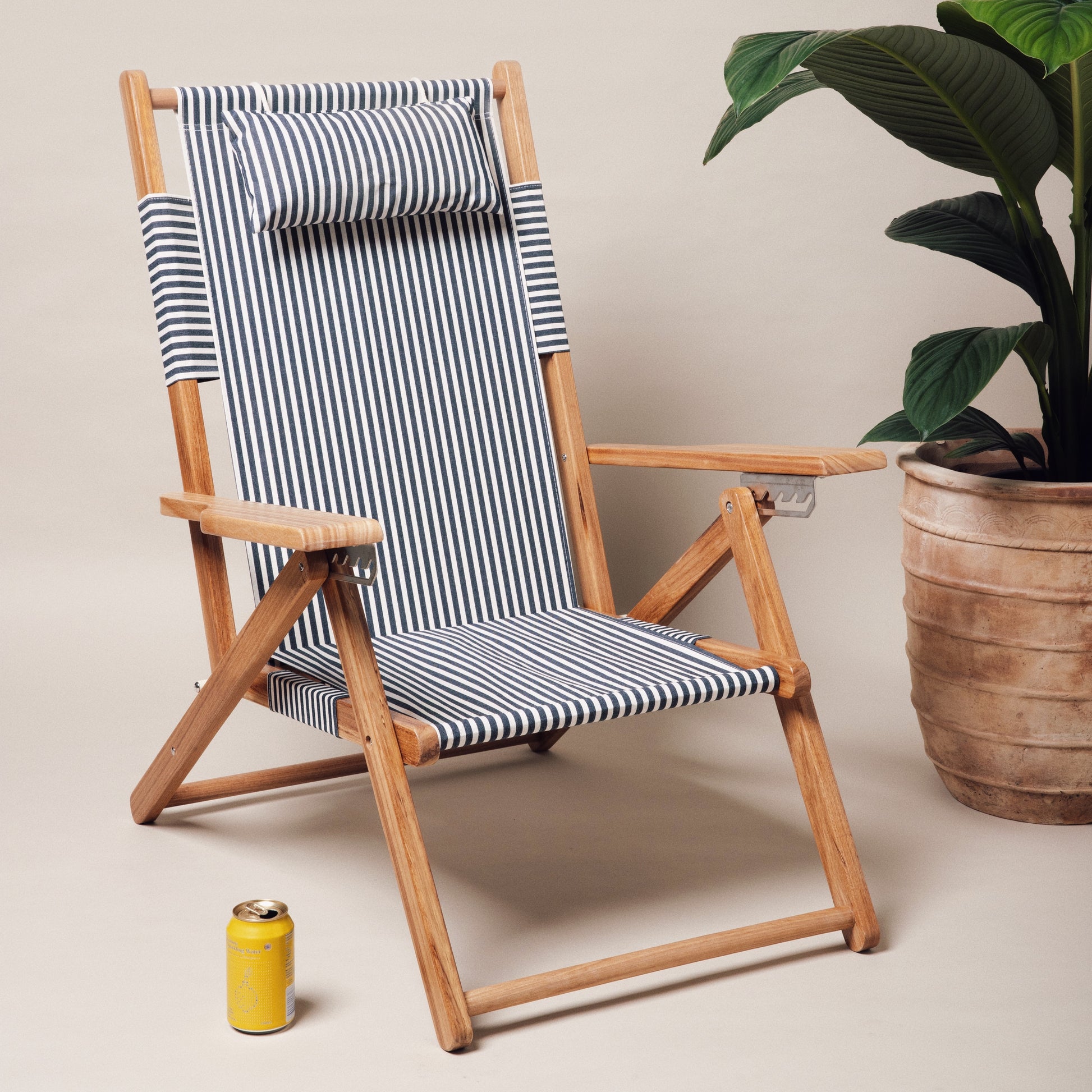 Navy and white stripe canvas reclining beach chair with teak frame and headrest.