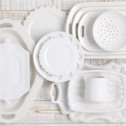 White ceramic Nonna serving platter with decorative handles, shown with other white dinnerware.