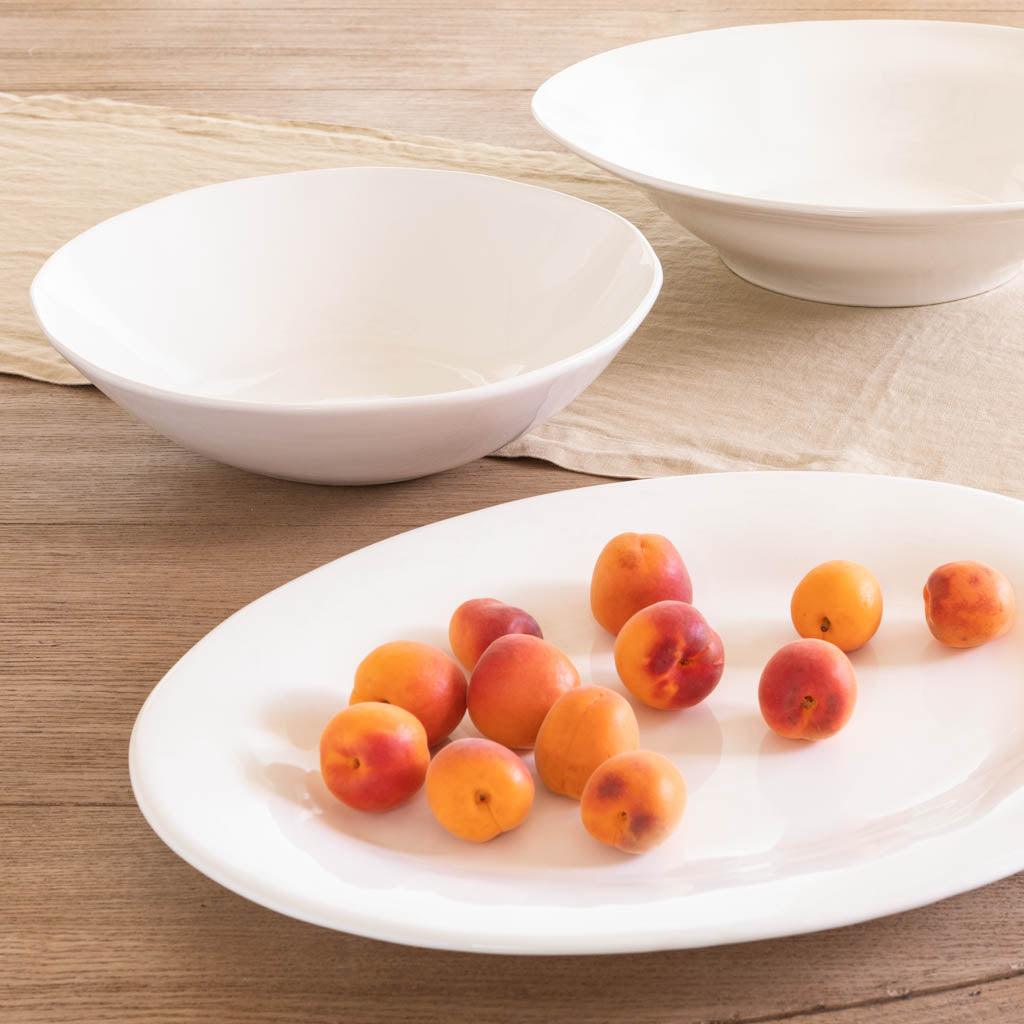 Creamy white Italian ceramic serving bowl with subtle organic edges, 16" diameter, on a wooden surface with fruit.