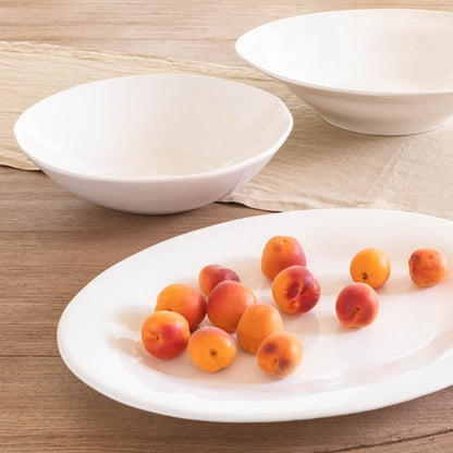 Creamy white Italian ceramic serving bowl with subtle organic edges, 16" diameter, on a wooden surface with fruit.