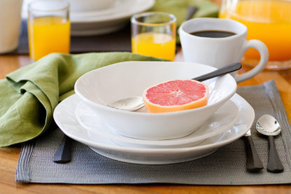White ceramic mug with subtle organic edges and creamy white glaze, part of a breakfast setting.