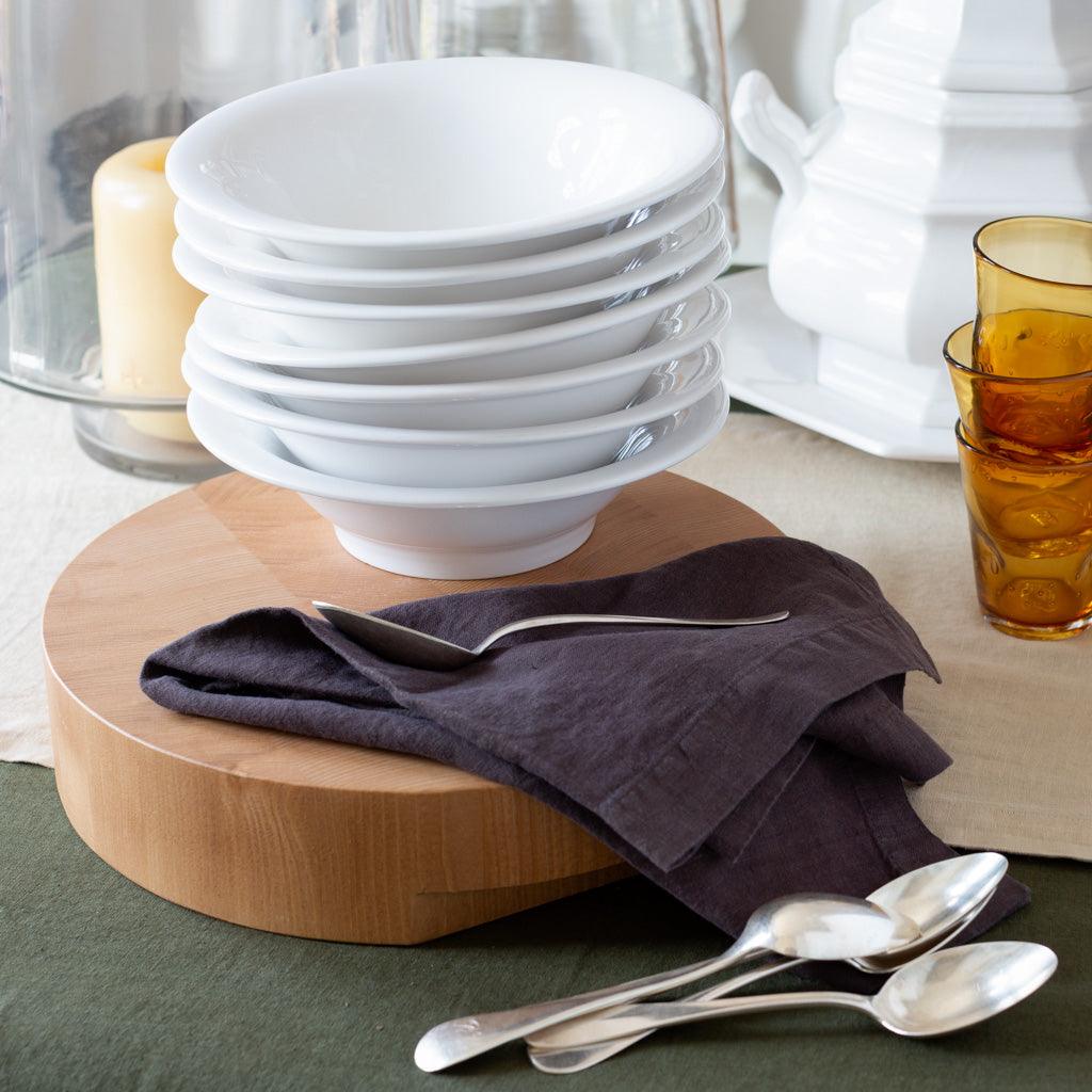 Stack of white ceramic HG Original individual bowls on a wooden board with a dark napkin and spoons.