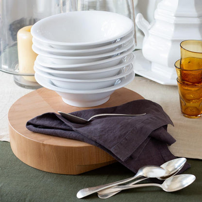 Stack of white ceramic HG Original individual bowls on a wooden board with a dark napkin and spoons.