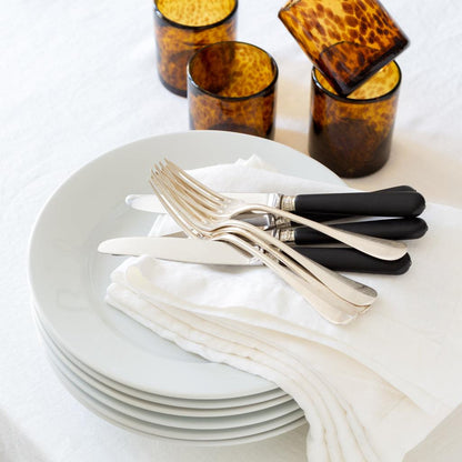 Stack of creamy white HG Original ceramic oversized dinner plates with silverware and amber glasses.