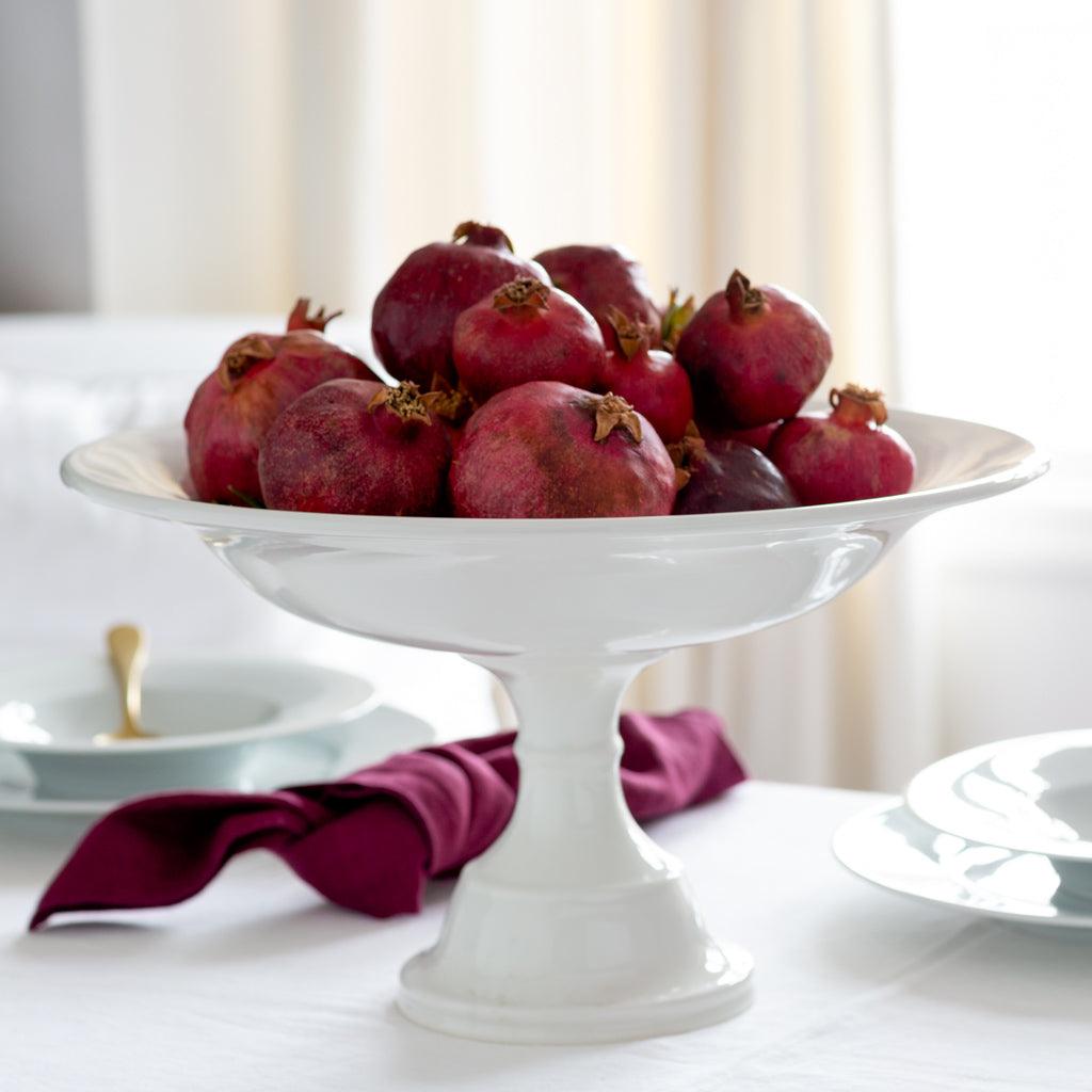 HG Original Pedestal Serve Bowl, creamy white ceramic, 15" Dia x 9" H, filled with pomegranates.