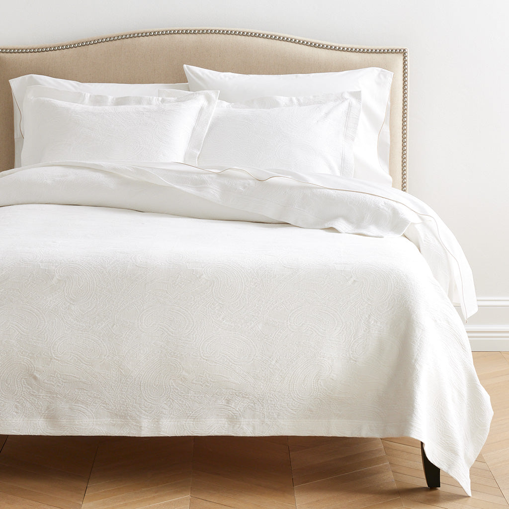 White cotton matelassé coverlet with subtle paisley pattern on a bed with matching shams.
