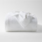 White cotton matelassé coverlet with subtle paisley pattern, folded on a white background.