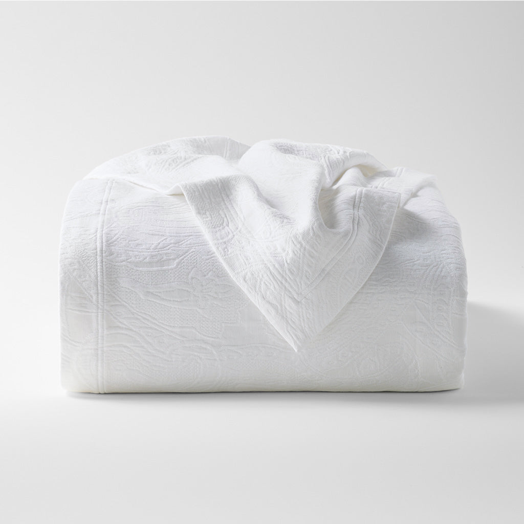White cotton matelassé coverlet with subtle paisley pattern, folded on a white background.