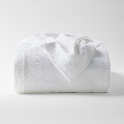 White cotton matelassé coverlet with subtle paisley pattern, folded on a white background.