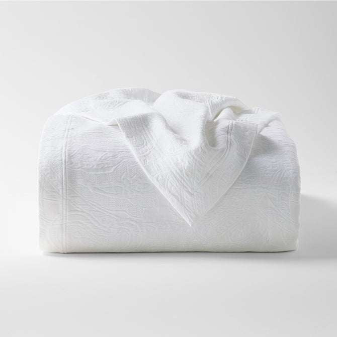 White cotton matelassé coverlet with subtle paisley pattern, folded on a white background.