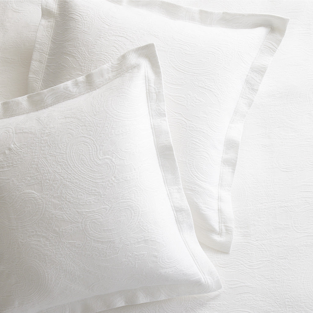 Two white cotton matelassé shams with subtle paisley pattern and 2-inch double-stitched hem.