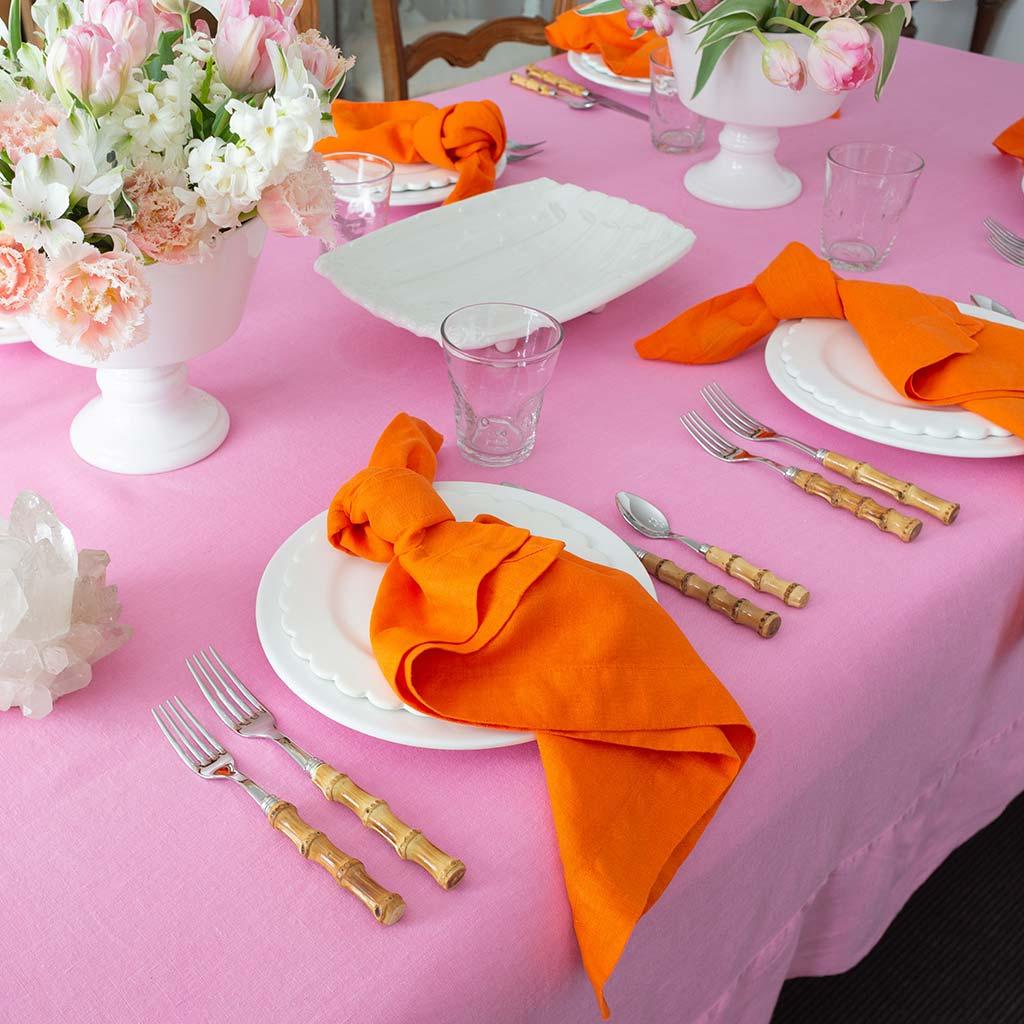 Persimmon HG Signature hand-dyed orange linen napkins, 22" square, knotted on white plates on a pink tablecloth.