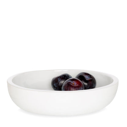 White ceramic serve bowl with three dark plums inside.