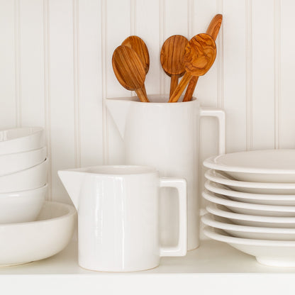 White ceramic rectangular handled pitcher with wooden spoons, bowls, and plates.