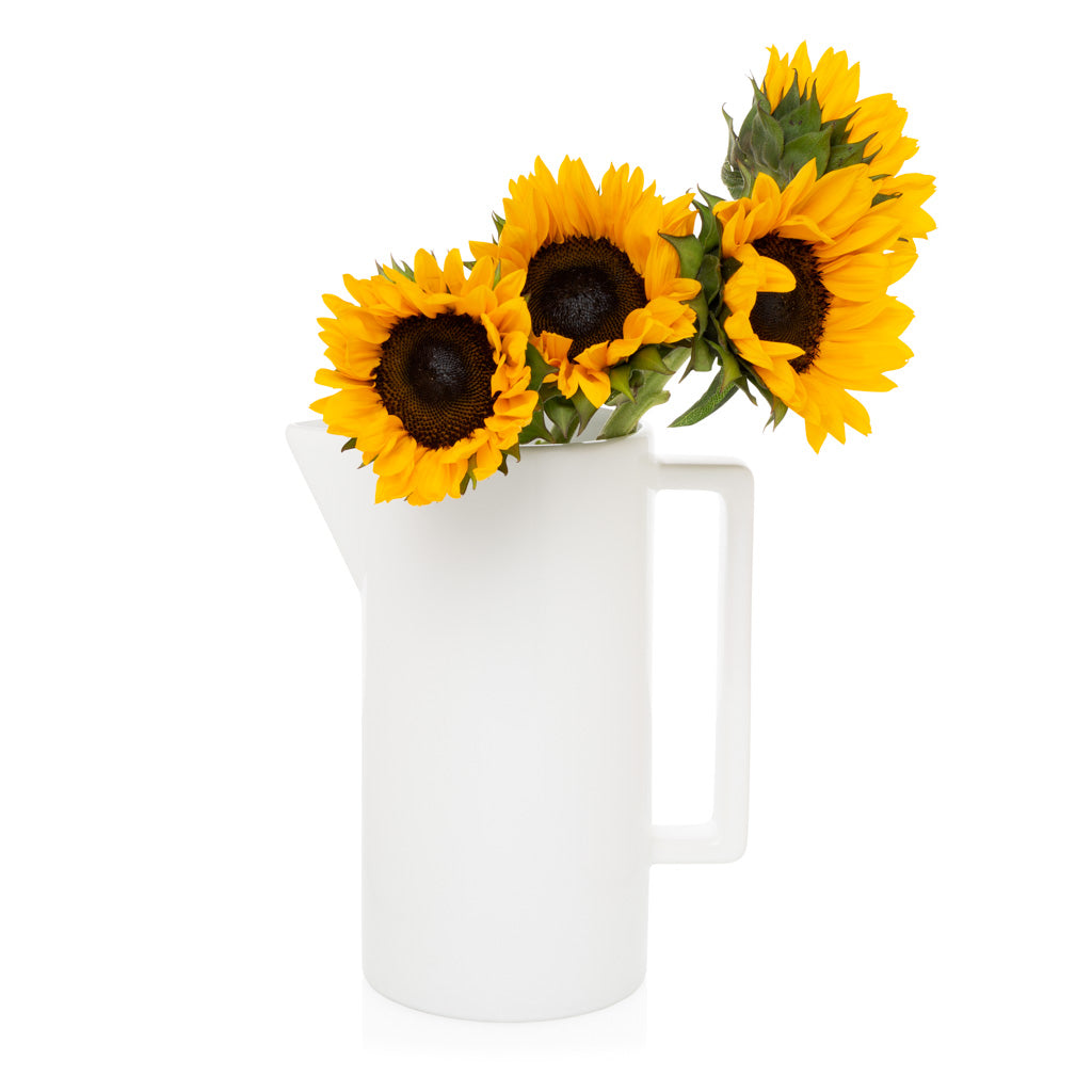 White rectangular ceramic pitcher with a handle, holding three bright yellow sunflowers.
