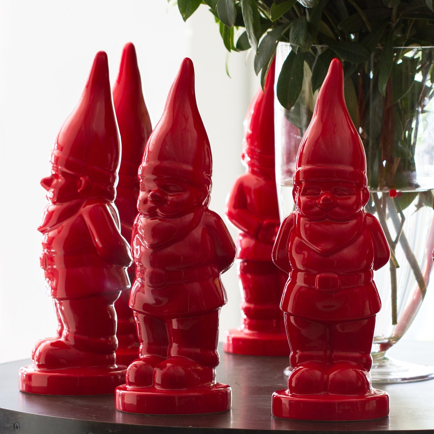 Five glossy red ceramic holiday gnomes with pointed hats, standing on a dark surface.