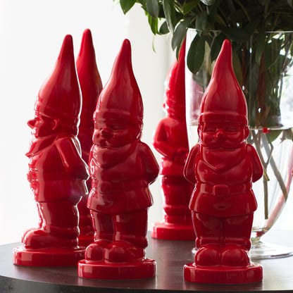 Five glossy red ceramic holiday gnomes with pointed hats, standing on a dark surface.