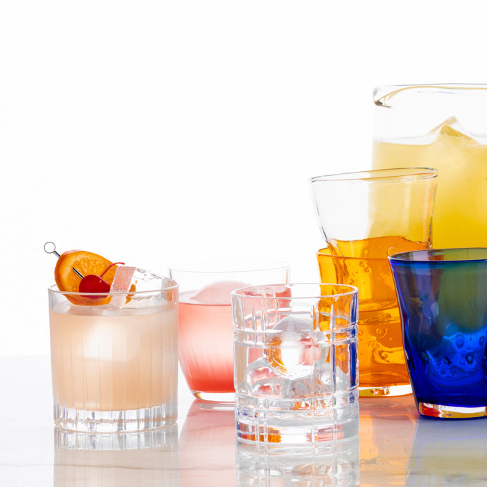 Clear Regent Eco-Crystal Double Old-Fashioned glass with ice, surrounded by other colorful drinkware.