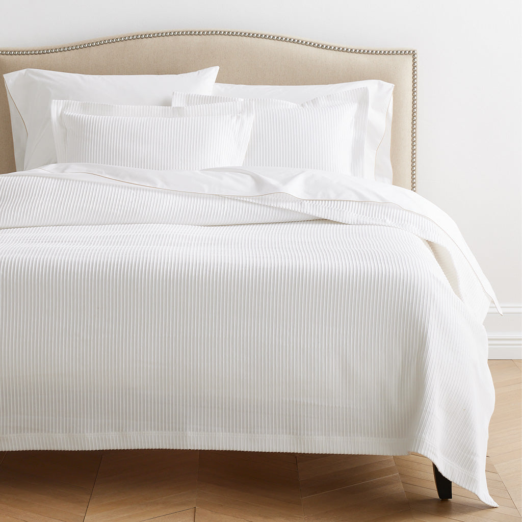 White ribbed cotton matelassé coverlet on a bed with matching shams and a beige upholstered headboard.