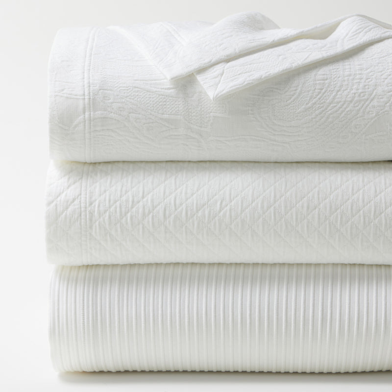 Stacked white ribbed cotton matelassé coverlet with subtle patterns and texture.