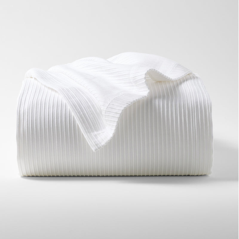 Folded white ribbed cotton matelassé coverlet with subtle texture.