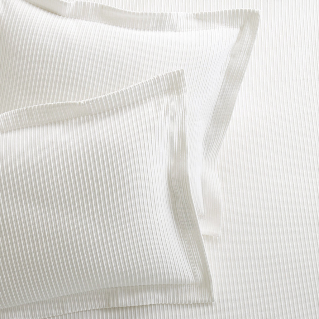 Two white ribbed cotton matelassé pillow shams with a 2" hem and mitered corners.
