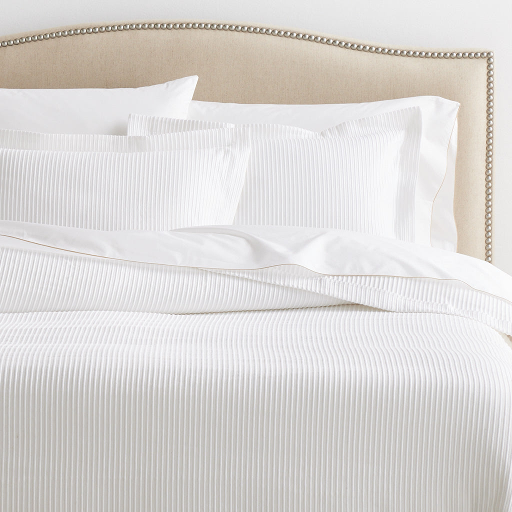 Two white ribbed cotton Matelassé pillow shams on a bed with a studded beige headboard.