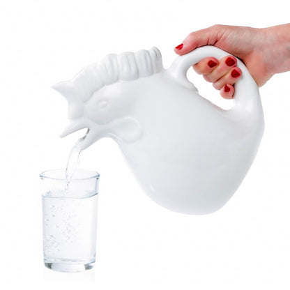 Hand pouring water from a white ceramic rooster pitcher into a clear glass.