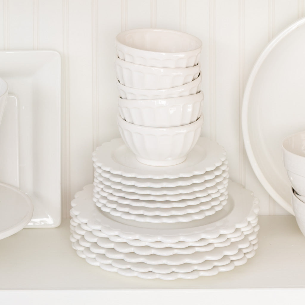 Stack of white ceramic scalloped salad plates and small bowls on a shelf.