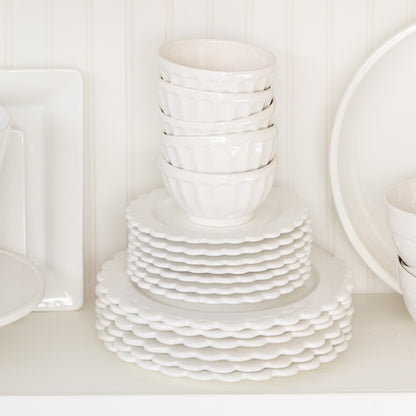 Stack of white ceramic scalloped salad plates and small bowls on a shelf.