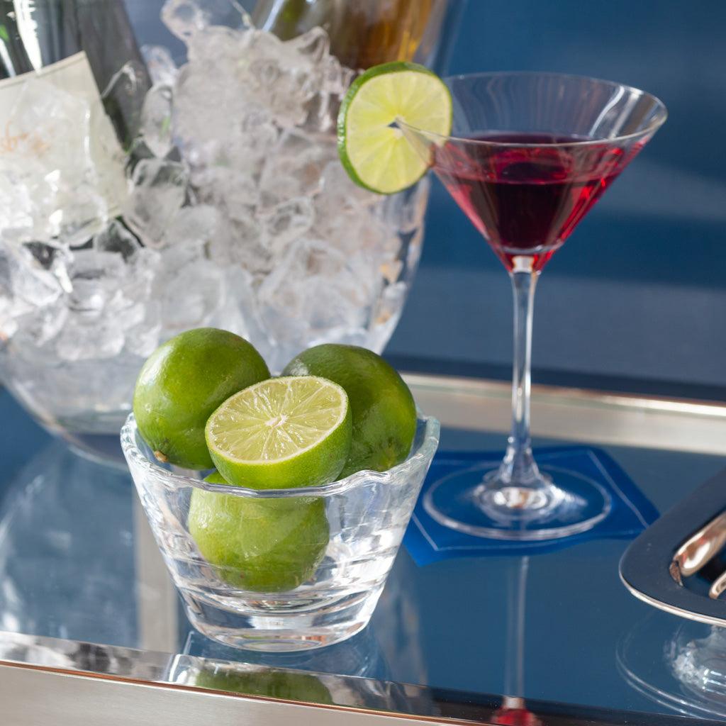 Clear, mouthblown glass breakfast bowl with scissor-cut top, holding whole and halved limes.